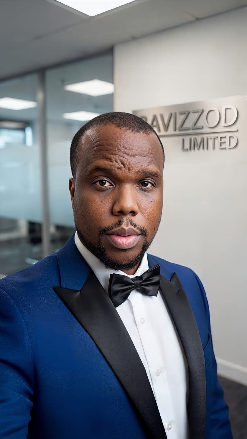 A Black man in a blue tuxedo and black bowtie posing in a modern office.